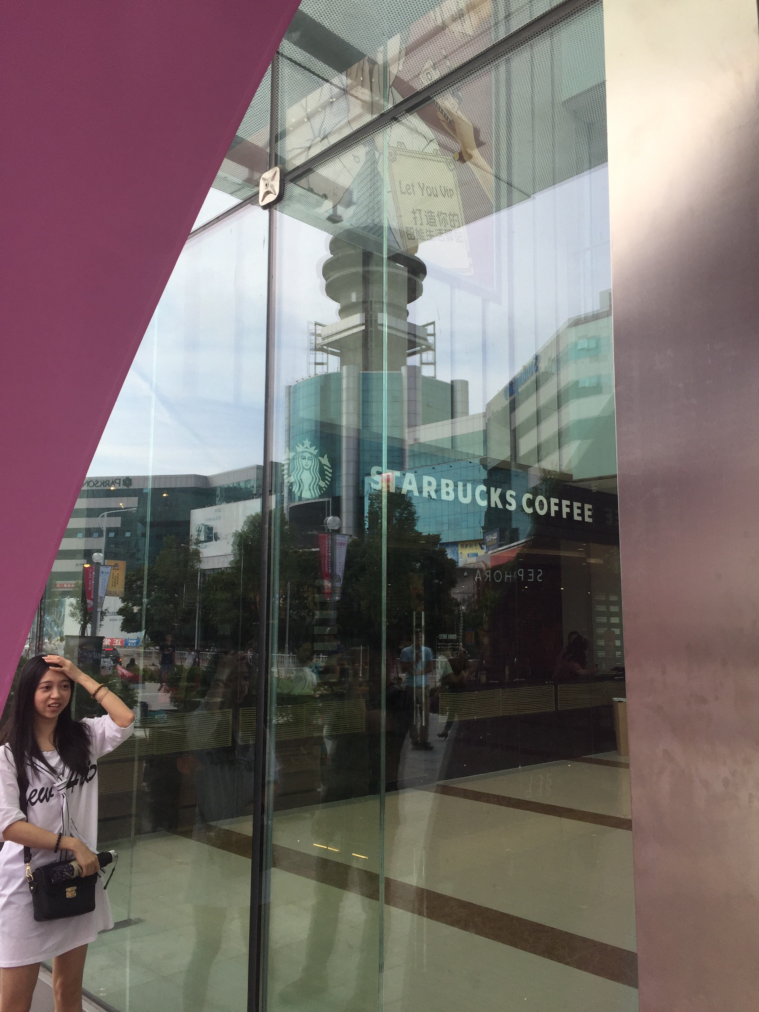 A woman stands outside of Suning Starbucks, with the reflection of “Old Walmart,” the Nanguo Shangcheng mall, reflected in the window. Photo: MyShantou.net