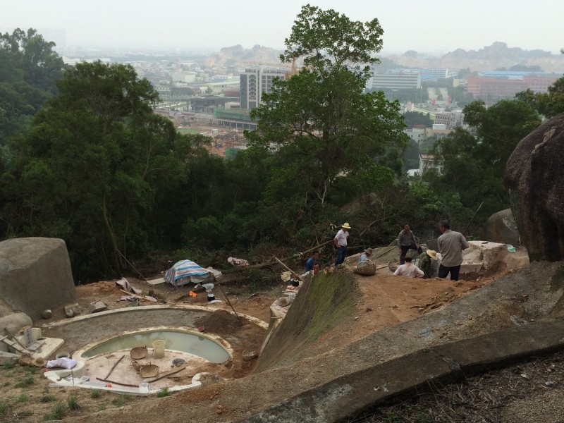 A view of graves under construction with cut trees in the middle background. In the far background, construction of Guangdong Technion is underway. Photo: Liang Yaoxiang